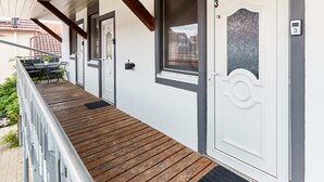 A wooden deck leading to a white door with a number plate, a small table with chairs, and a window with frosted glass. - Schönes Zimmer mit Bad - nur 10 Gehminuten vom Europa-park (Rust)
