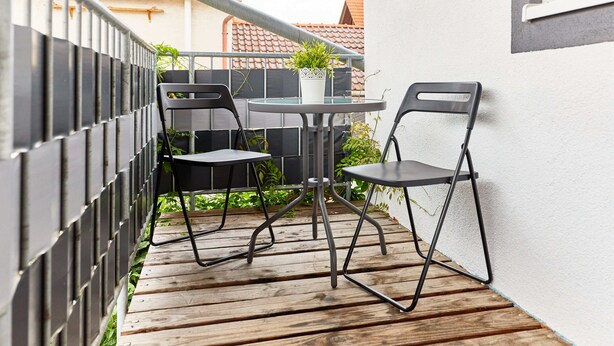 A small outdoor patio with a round table and two chairs, a potted plant, and a wooden deck. - Schönes Zimmer mit Bad - nur 10 Gehminuten vom Europa-park (Rust)