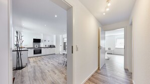 Een moderne keuken met witte kasten, een zwart aanrecht en een eethoek met een witte tafel en stoelen.