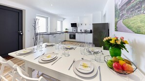 Een moderne keuken met witte kasten, een eethoek voor vier personen met witte stoelen, en een fruitschaal op de tafel.