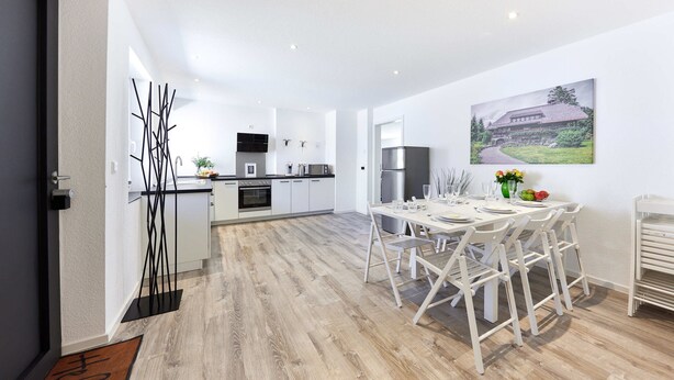 Een moderne keuken met witte kasten, een roestvrijstalen koelkast, en een eethoek met een witte tafel en stoelen.