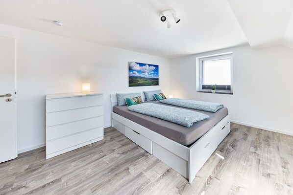 A bedroom with a bed, a dresser, a window, and a painting on the wall.