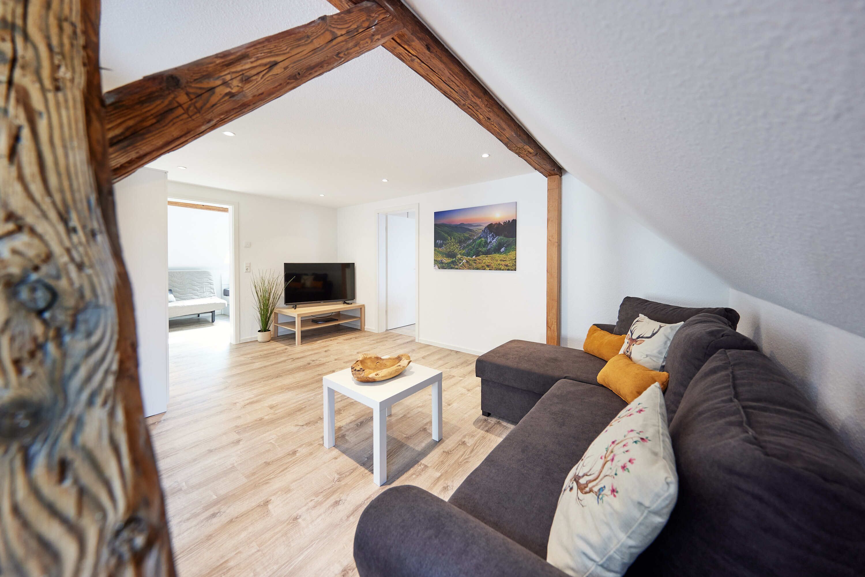 Ett modernt vardagsrum med ett träpanelat tak, en grå soffa, ett vitt soffbord och en tavla på väggen.