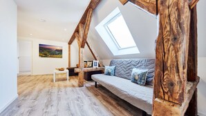 Ein Schlafzimmer im Loftsstil mit freiliegenden Holzbalken, einem Oberlicht, einem grauen Sofa und einem Gemälde an der Wand.