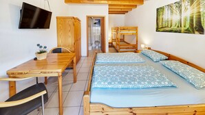 Ein Zimmer mit zwei Etagenbetten, einem Holztisch mit Stuhl, einem an der Wand befestigten Fernseher und einem Waldgemälde.
