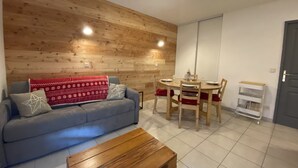 Een woonkamer met een bank, een salontafel, een eettafel met stoelen en een houten wand.