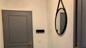 Een gang met een grijze deur, een klein bankje, een spiegel aan de muur en een stopcontact.