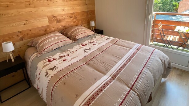 Een slaapkamer met een houten hoofdbord, een groot bed met beddengoed met een patroon, een bedlampje en uitzicht op een balkon met een leuning.