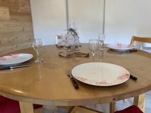 A round wooden dining table with a white plate featuring red floral patterns, a fork, and a knife. - Cozy Apartment with a Mountain View (Briançon)
