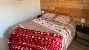 Een slaapkamer met een houten hoofdeinde, een bed met beddengoed met een patroon, twee wandlampen en twee ingelijste posters aan de muur.
