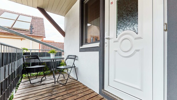 A wooden deck with a table and chairs, a white door with a decorative glass panel, and a metal railing. - Beautiful room perfect for families - only 10 minutes walk from Europa-Park (Rust)