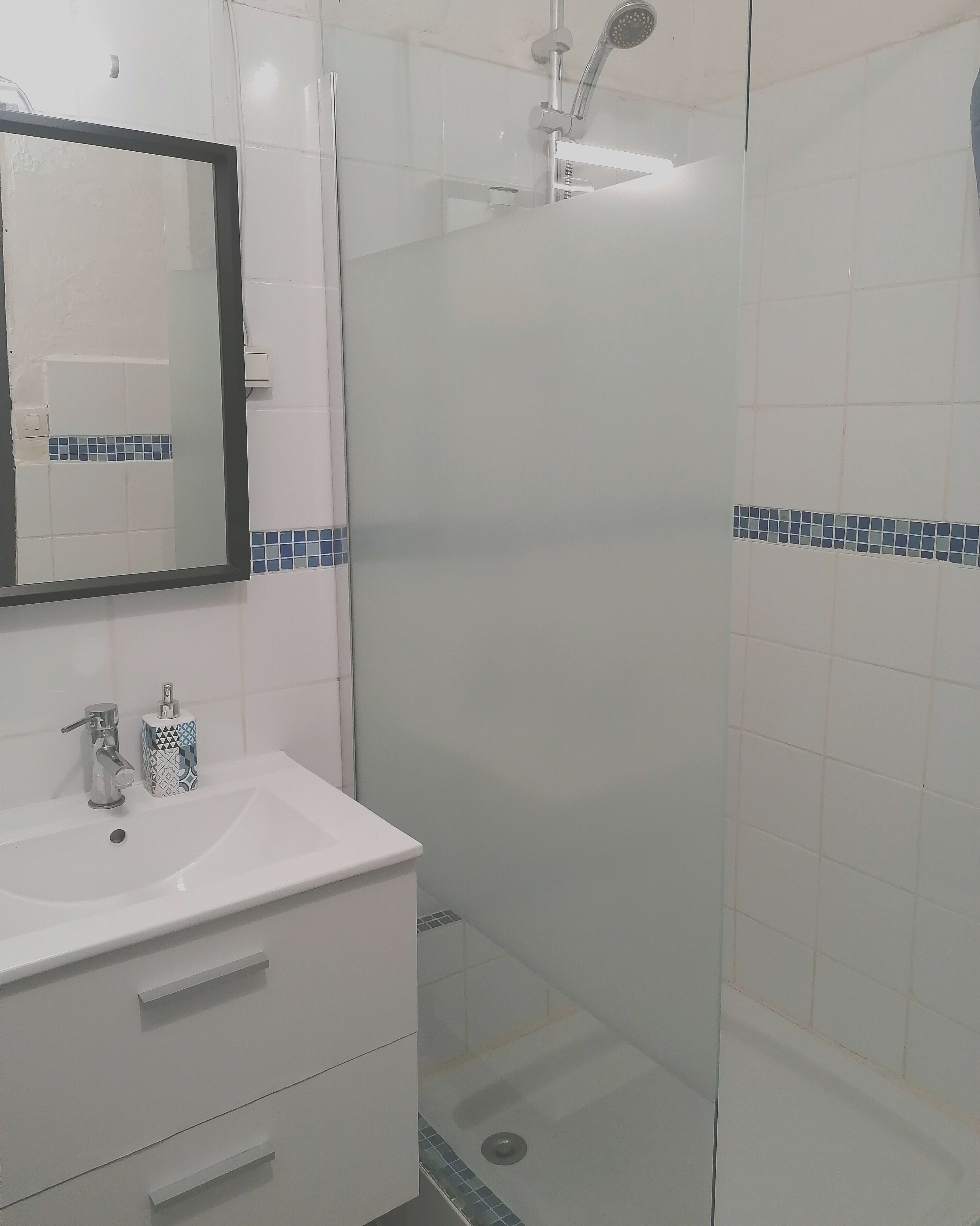 Une salle de bain avec un lavabo blanc, un miroir, une douche et des murs recouverts de carreaux bleus.