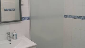 Une salle de bain avec un lavabo blanc, un miroir, une douche et des murs recouverts de carreaux bleus.