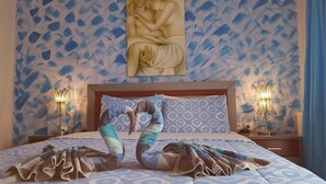 Habitación de hotel con pared estampada, cama con colcha azul y blanca, dos almohadas decorativas y dos lámparas de noche.