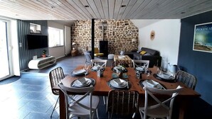A dining area with a stone wall, a wooden ceiling, and a modern kitchen in the background.