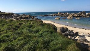 A coastal landscape with a sandy beach, rocky outcrops, and a clear blue sky.