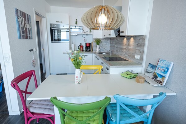 A modern kitchen with white cabinetry, a built-in oven, a coffee maker, and a hanging pendant light.