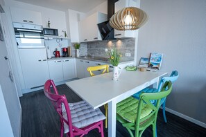 A modern kitchen with white cabinets, a built-in oven, and a microwave. There is a dining table with colorful chairs and a vase with flowers.