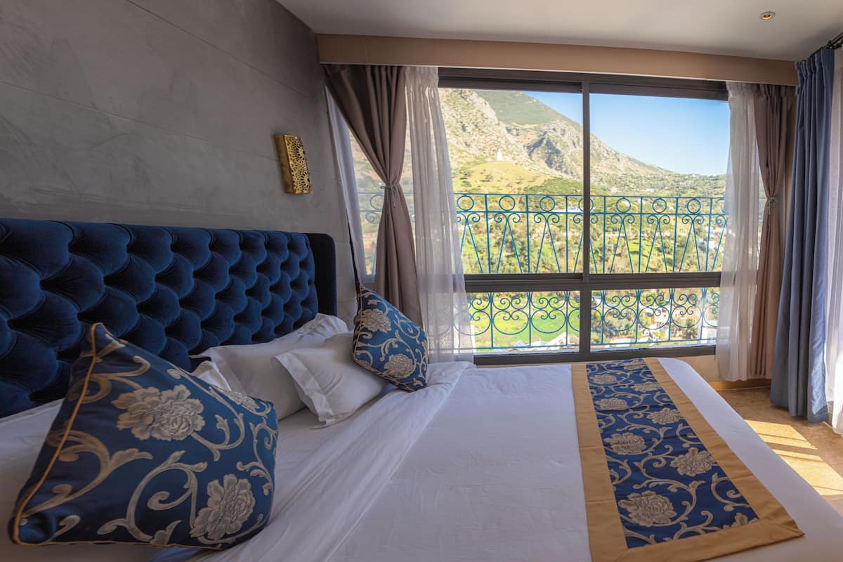 A bedroom with a large bed, a view of a mountainous landscape through a balcony.