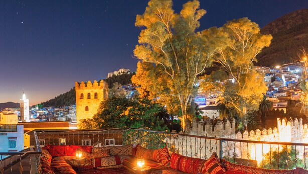 A rooftop terrace with a view of a historic building and a tree. - VANCII HOTEL (Chefchaouen)
