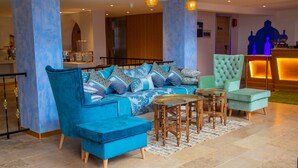 A modern lobby with a blue sofa set, a green armchair, and a wooden coffee table. - VANCII HOTEL (Chefchaouen)