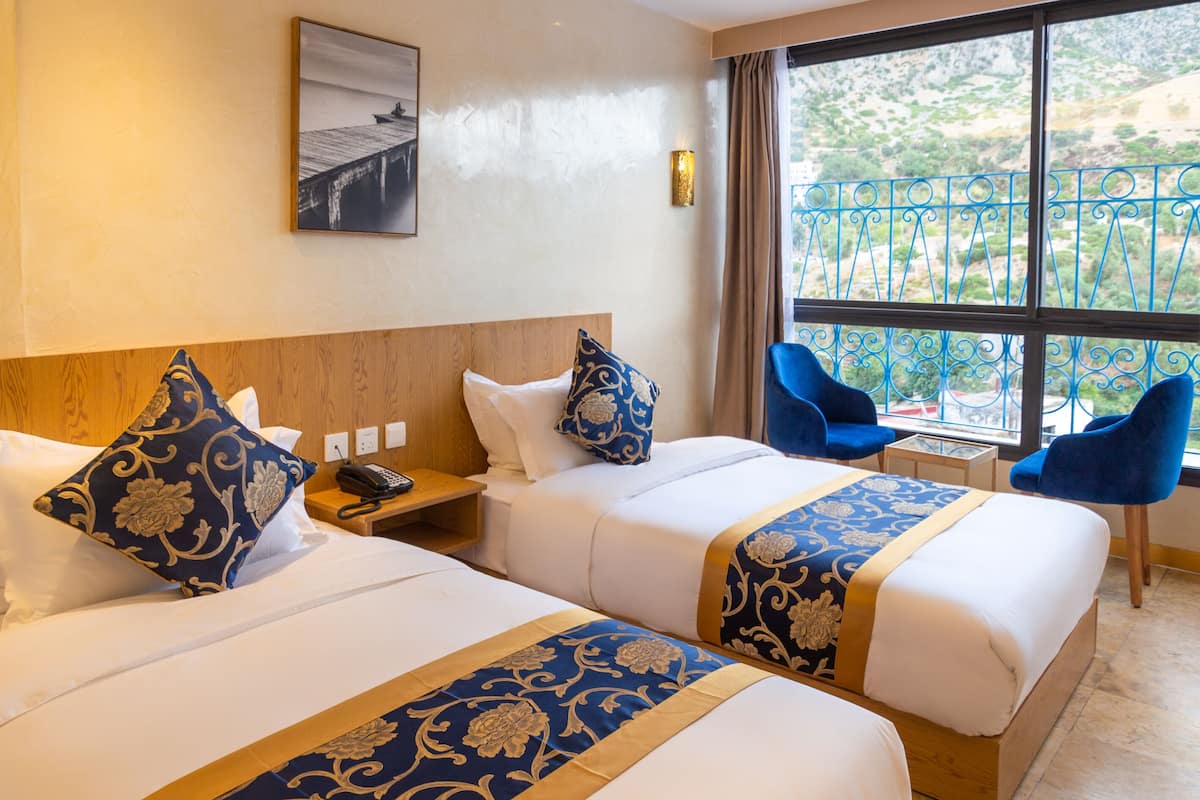 A hotel room with two beds, a nightstand, a chair, and a large window with a view of the outdoors.