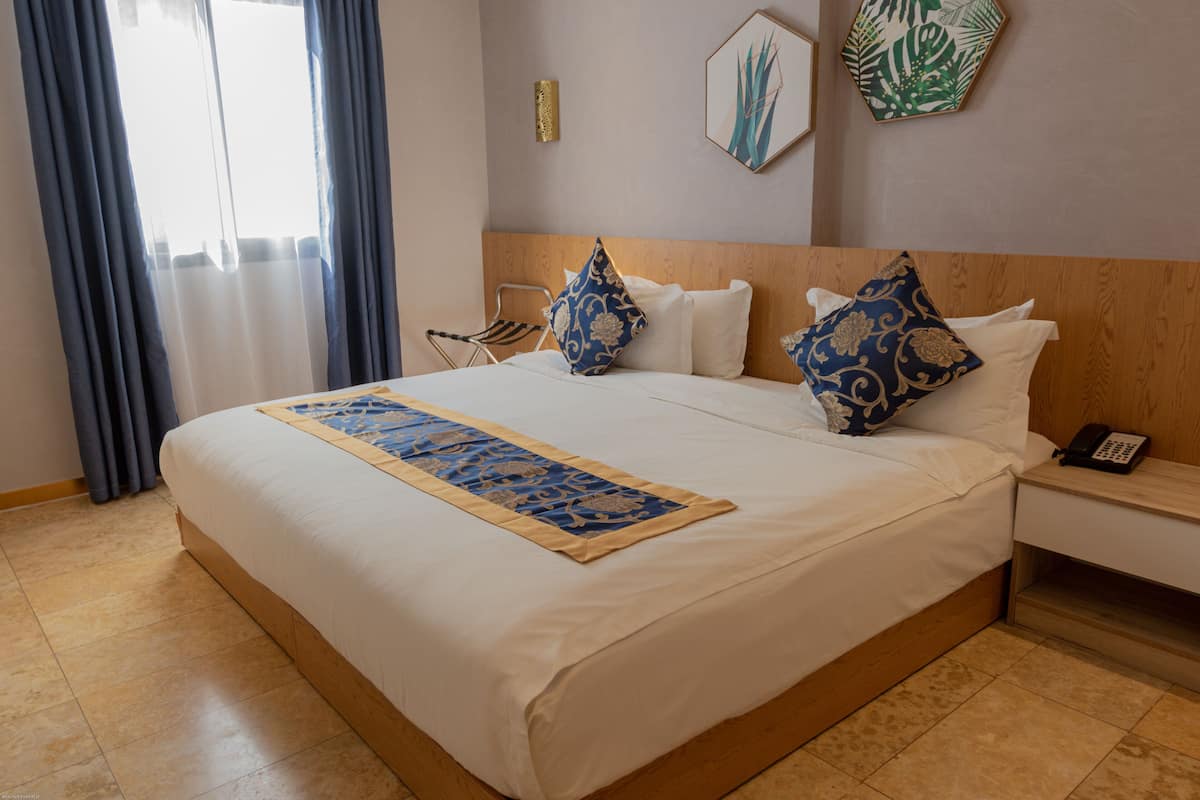 A hotel room with a large bed, a wooden headboard, a bedside table with a phone, and a window with curtains.