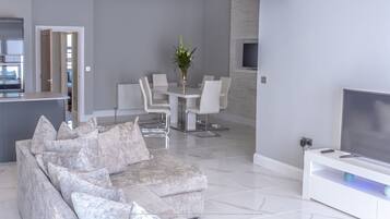 Una sala de estar moderna con un sofá gris, una mesa de comedor con sillas, un televisor y un jarrón con flores.