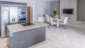A modern kitchen with a central island, built-in appliances, and a dining area with a white table and chairs. - 4 Bed-sleeps 8- Free Parking-pets-hot Tub (Kelty)