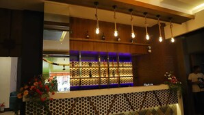 Un espace bar avec un mur décoré de motifs, des luminaires suspendus et un comptoir agrémenté d’une plante ornementale.