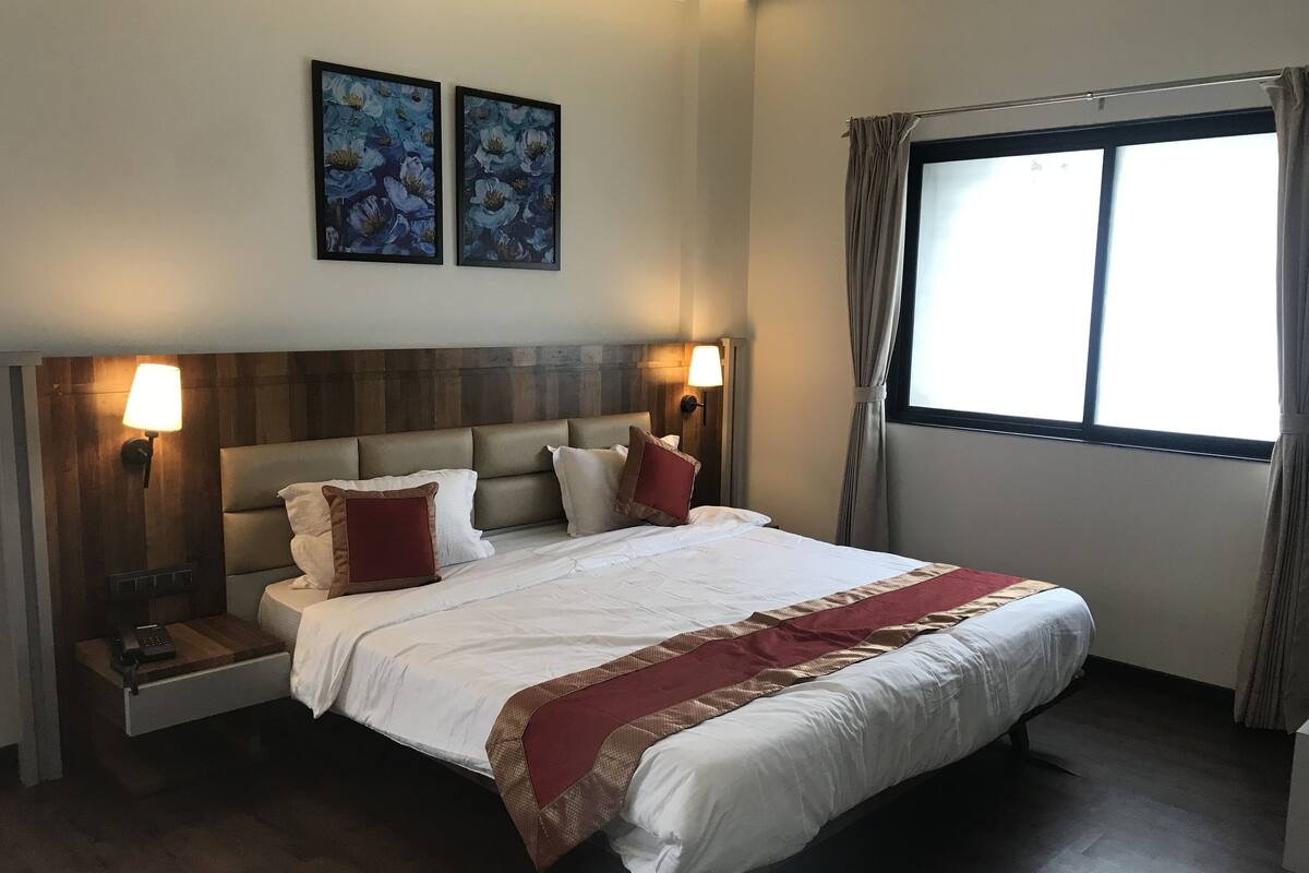 Una camera d'hotel con un grande letto, due lampade a parete, una finestra con tende e due quadri floreali incorniciati.