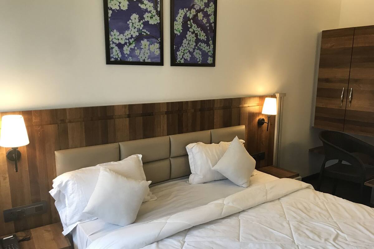 Camera d'albergo con un letto, due lampade a parete, una testiera in legno e due quadri floreali incorniciati.