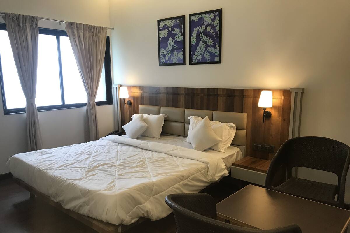 Una camera d'albergo con un letto grande, due lampade a parete, una testiera in legno e due opere d'arte floreali incorniciate.