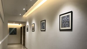 Un couloir dont les murs sont ornés d’œuvres d’art encadrées, avec un luminaire au plafond et une porte au bout.