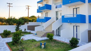 A modern building with a white and blue exterior, a staircase leading to the entrance, and a small garden area with potted plants and a decorative sculpture. - Pittas Studios Kardamena 300 Meters From the Beach (Kos)