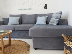 A grey sectional sofa with three cushions, a round wooden side table, and a woven rug.