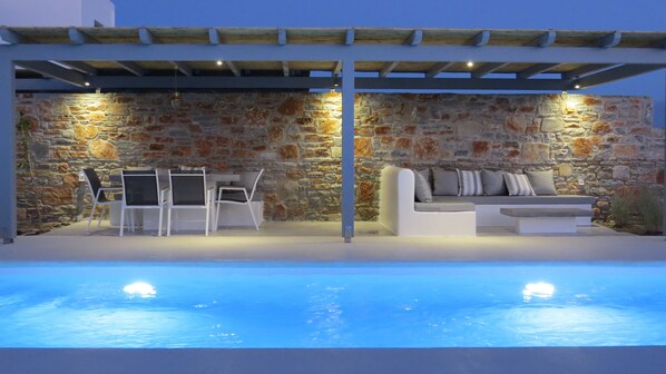 A poolside area with stone walls, a white sofa, and a table with chairs.
