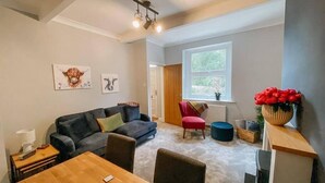 A modern living room with a grey sofa, a red chair, a wooden dining table, and a large window with a view of greenery. - LITTLE RED HOLIDAY HOME // Luxe 2 bed accommodation in Halifax // West Yorkshire (Luddenden)