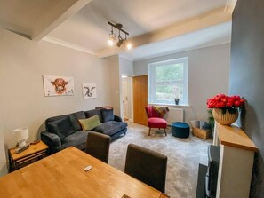 Relax in this stylish living area with a sofa, dining table, and armchair, surrounded by artwork and a view of lush greenery.
