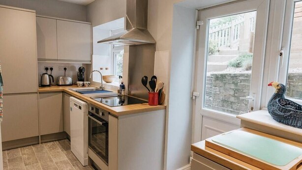 A compact kitchen with a dishwasher, oven, and a window with a view of the street. - LITTLE RED HOLIDAY HOME // Luxe 2 bed accommodation in Halifax // West Yorkshire (Luddenden)