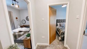 A bedroom with a bed, bedside table, and a mirror. There is a door leading to another room. - LITTLE RED HOLIDAY HOME // Luxe 2 bed accommodation in Halifax // West Yorkshire (Luddenden)