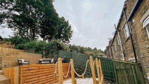 A wooden deck with a stone-tiled patio, surrounded by a green fence and a stone wall. - LITTLE RED HOLIDAY HOME // Luxe 2 bed accommodation in Halifax // West Yorkshire (Luddenden)