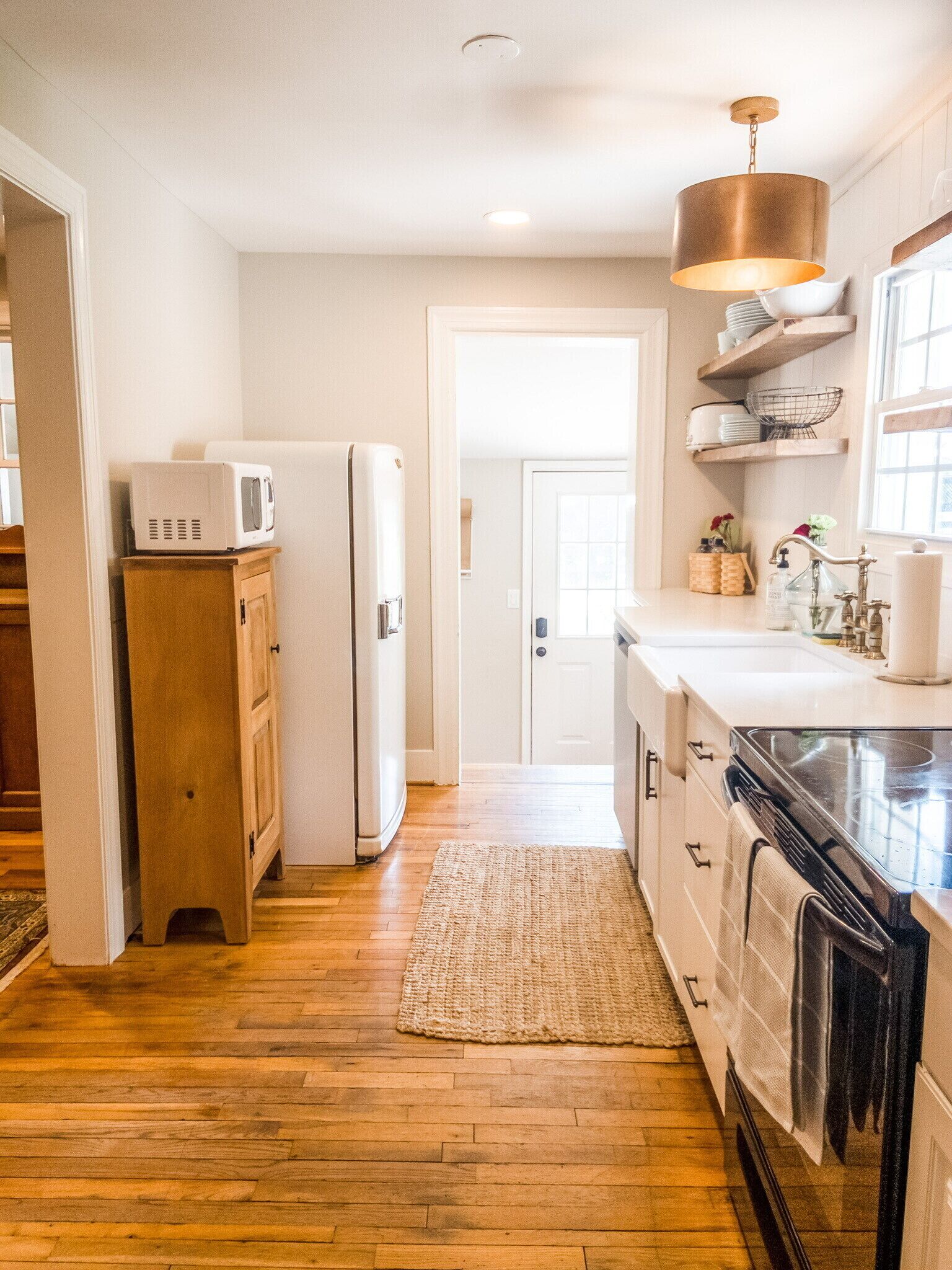 A kitchen with wooden flooring, white cabinets, a black oven, a microwave, and a hanging light fixture.