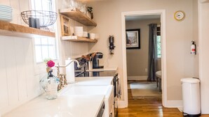 A modern kitchen with white cabinetry, wooden shelves, and a stainless steel range hood. - Littlefield Cottage  (Middleburg)