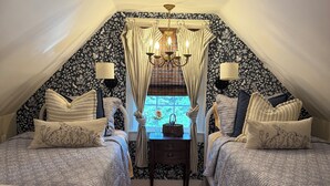A cozy attic bedroom with two beds, a chandelier, and a window with curtains. - Littlefield Cottage  (Middleburg)