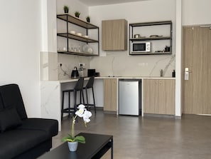 A modern kitchen with built-in appliances, a dining area with a black table and chairs, and a black sofa in a living room area.