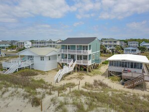 A beachfront property with multiple houses, some elevated on stilts, and a sandy beach area. - Experience oceanfront living at the spacious 5-bedroom Pilot House in Oak Island, NC. (Oak Island)