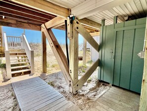 A wooden structure with a staircase leading to a deck, a green door, and a sandy ground.