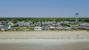 A coastal residential area with houses on stilts, a water tower, and a beach.