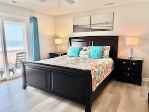 A bedroom with a bed, two nightstands, a headboard, a window with a view, and a door.